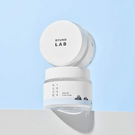 Round Lab 1025 Dokdo Cream jar with minimalist design, white lid, and mountain graphic on label against light blue background
