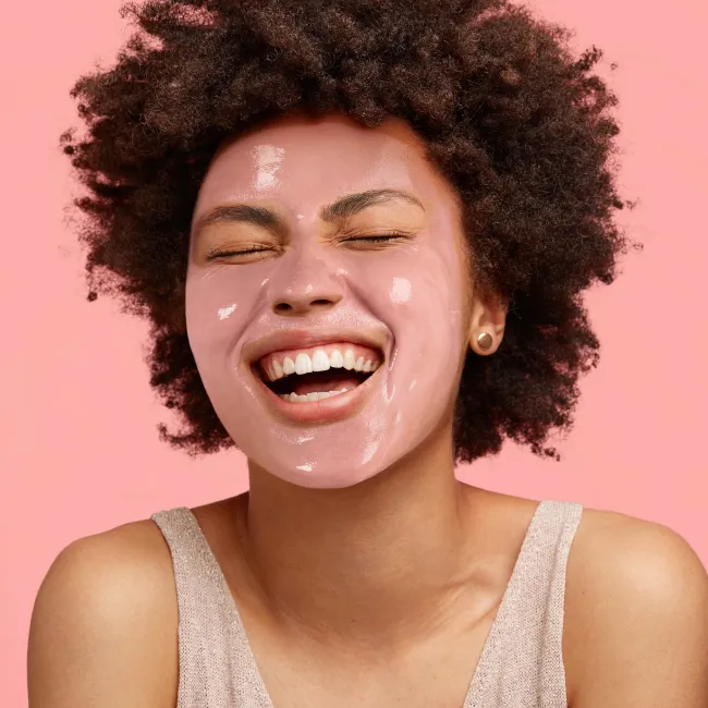 Pink peel-off mask applied on face, smiling model with product still visible