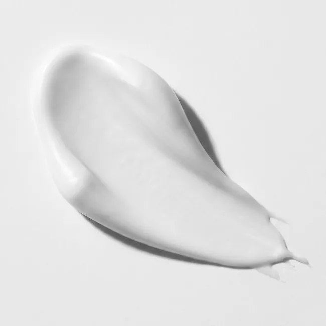 A smooth, creamy white product smear, likely a cosmetic cream or lotion, spread on a clean, light gray background with a soft shadow.