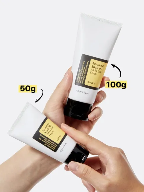 Hands holding 50g and 100g tubes of COSRX Advanced Snail 92 All In One Cream; dual-size options for travel and full use, featuring same 92% snail mucin formula that delivers hydration, elasticity, and slow-aging benefits for glowing, glass-like skin.