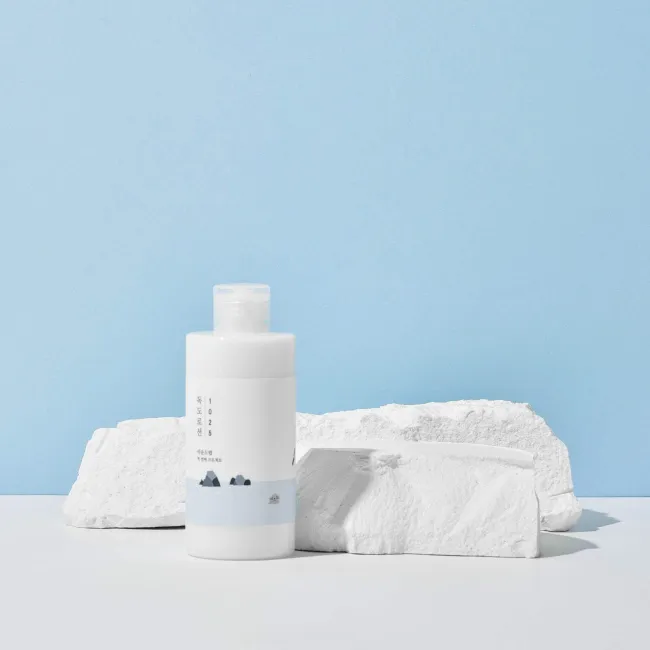 Clean skincare toner bottle with minimalist design, set against light blue background with white stone accents