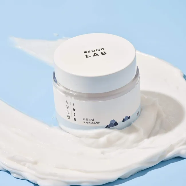 Round Lab 1025 Dokdo Cream jar with creamy texture swatch on blue background, clean skincare from Korea