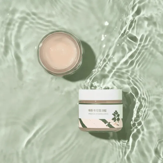 Gentle pink skincare cream in glass jar with Korean label, floating on rippling water surface, clean beauty aesthetic
