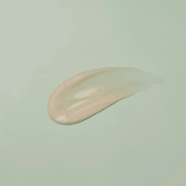 Smooth, creamy beige skincare product swatch on soft green background, showcasing clean K-Beauty texture