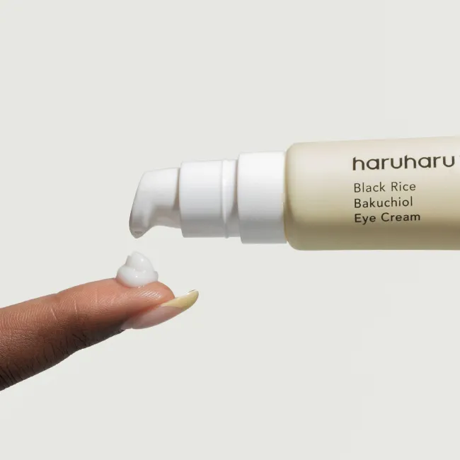 A close up of A tube of BLACK RICE bakuchiol eye cream for reduced appearance of fine lines and wrinkles for sensitive skin being pumped on a finger