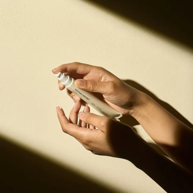 A close up of two hand pumping a tube of BLACK RICE bakuchiol eye cream for reduced appearance of fine lines and wrinkles for sensitive skin into her finger