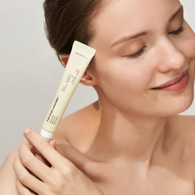 A close-up of a woman’s face after using BLACK RICE Bakuchiol Eye Cream, showing a reduced appearance of fine lines and wrinkles on sensitive skin, alongside a tube of the product.