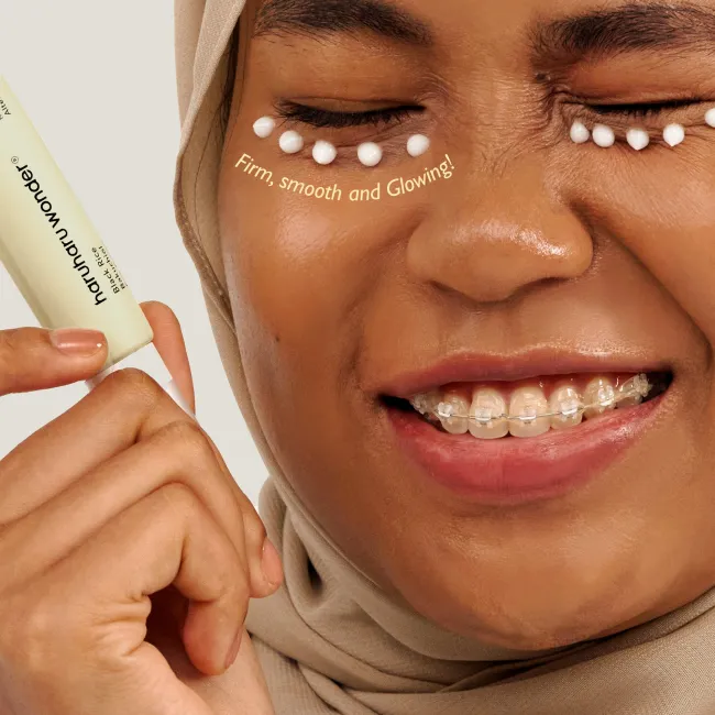 A close up of a face of a woman applied and dotted A tube of BLACK RICE bakuchiol eye cream for reduced appearance of fine lines and wrinkles for sensitive skin around her eyes with benefits such as firm, smooth and glowing highlighted