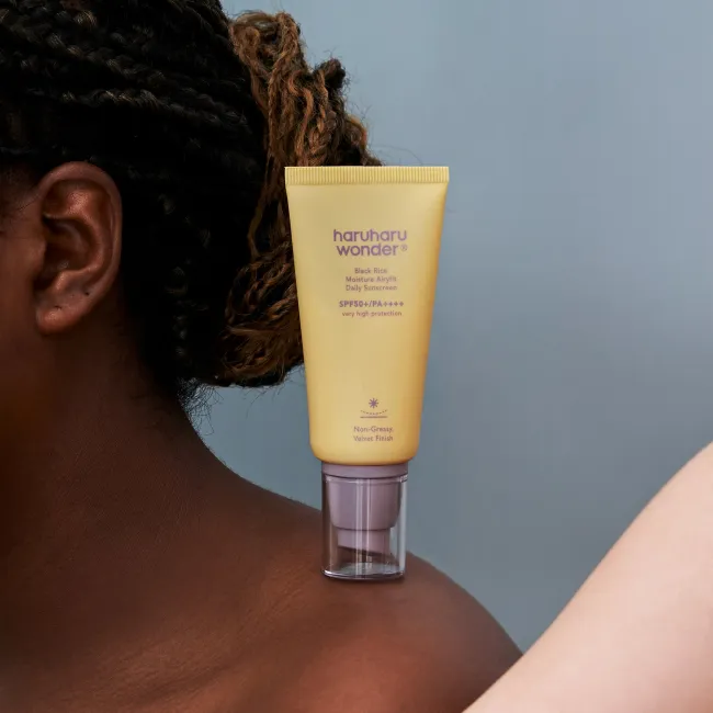 A close up of a woman with  BLACK RICE moisture airyfit daily sunscreen with SPF50+ PA++++ by haruharu wonder with very protection non-greasy, velvet finish on her shoulder.