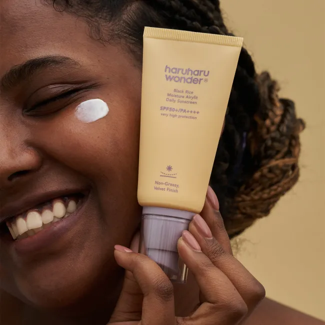 A close up of a woman applied  BLACK RICE moisture airyfit daily sunscreen with SPF50+ PA++++ by haruharu wonder with very protection non-greasy, velvet finish on her face and showing the product