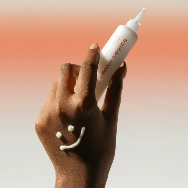 A close up of a hand holding A tube of Centella 5% Niacinamide Radiance  Gel Cream 40g on a white and orange background.