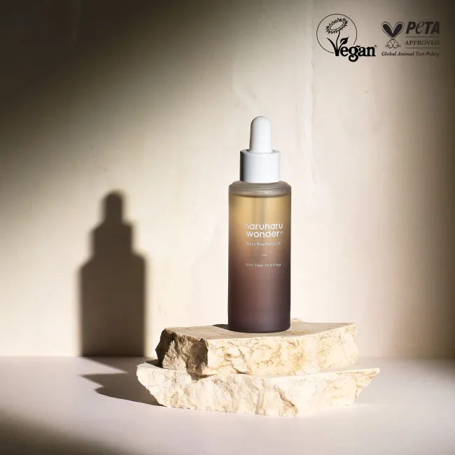 haruharu wonder black rice facial oil dropper bottle on a stone surface with a neutral background, featuring PETA Vegan approval logo