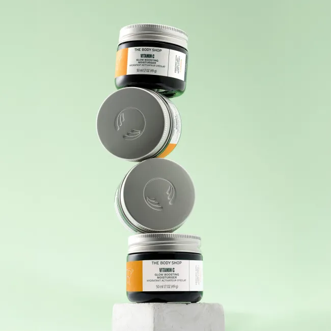 Stack of The Body Shop Glow Boosting Moisturiser jars on a light green background
