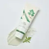 Korean skincare cleanser tube with green leaf design, creamy texture swatch, and fresh herb on white background