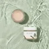 Gentle pink skincare cream in glass jar with Korean label, floating on rippling water surface, clean beauty aesthetic