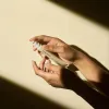 A close up of two hand pumping a tube of BLACK RICE bakuchiol eye cream for reduced appearance of fine lines and wrinkles for sensitive skin into her finger